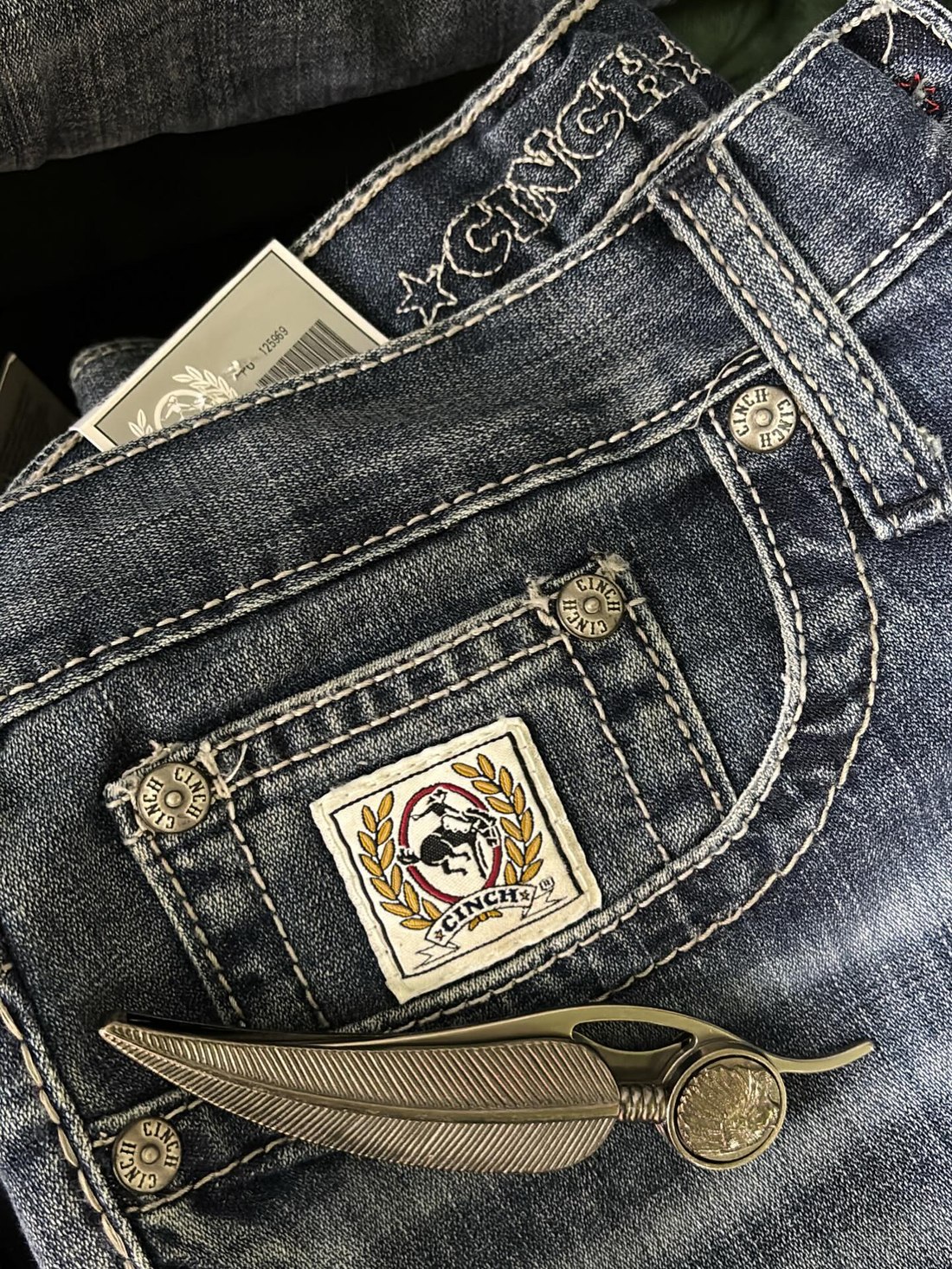 Detalhe macro de jeans com bolso, rebites e etiqueta bordada da marca Cinch