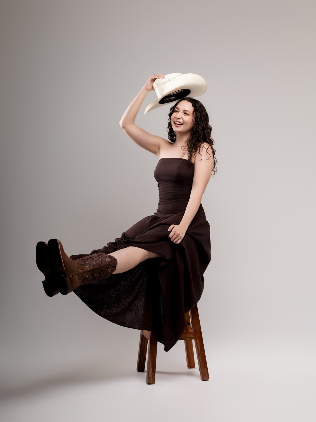 Mulher sorrindo com chapéu country branco, vestido midi marrom e bota de cano curto